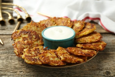 Photo of Delicious potato pancakes, sour cream, menorah and candles on wooden table, closeup. Hanukkah festive food