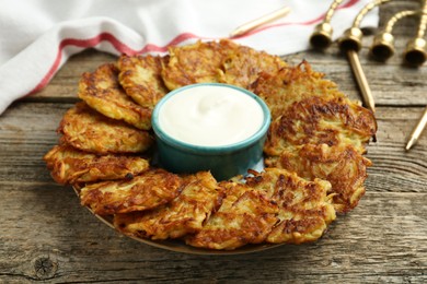 Photo of Delicious potato pancakes, sour cream, menorah and candles on wooden table, closeup. Hanukkah festive food