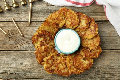 Photo of Delicious potato pancakes, sour cream, menorah and candles on wooden table, flat lay. Hanukkah festive food