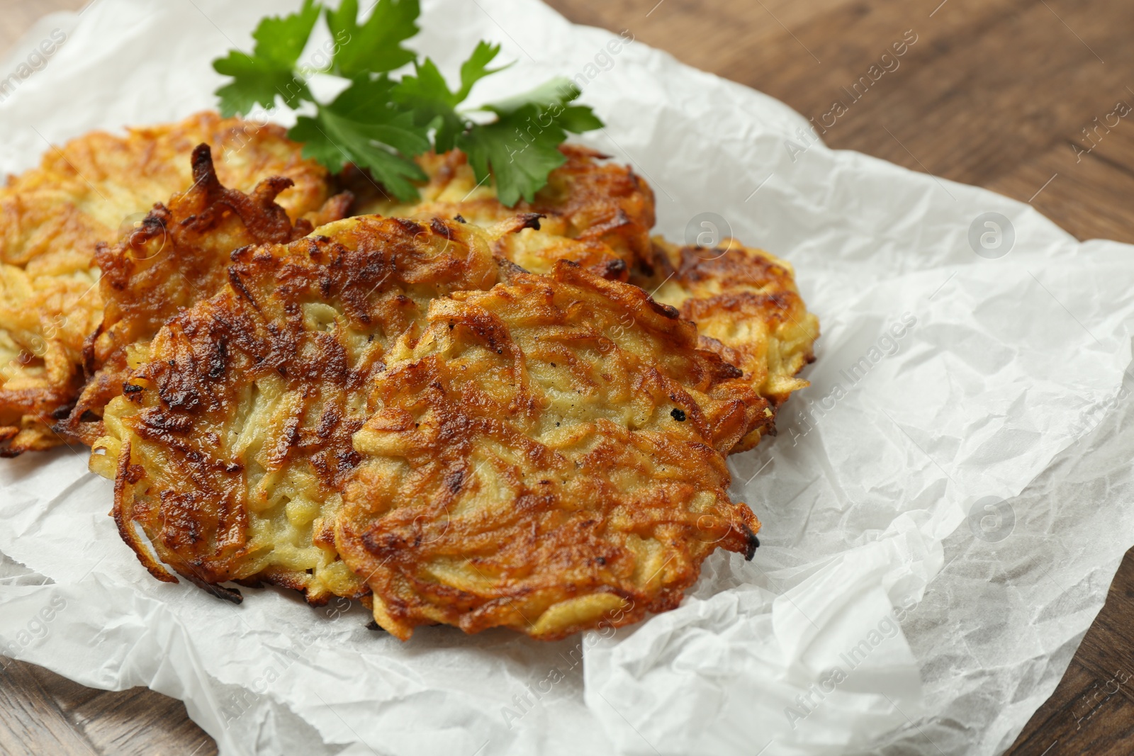 Photo of Delicious potato pancakes and parsley on wooden table, closeup