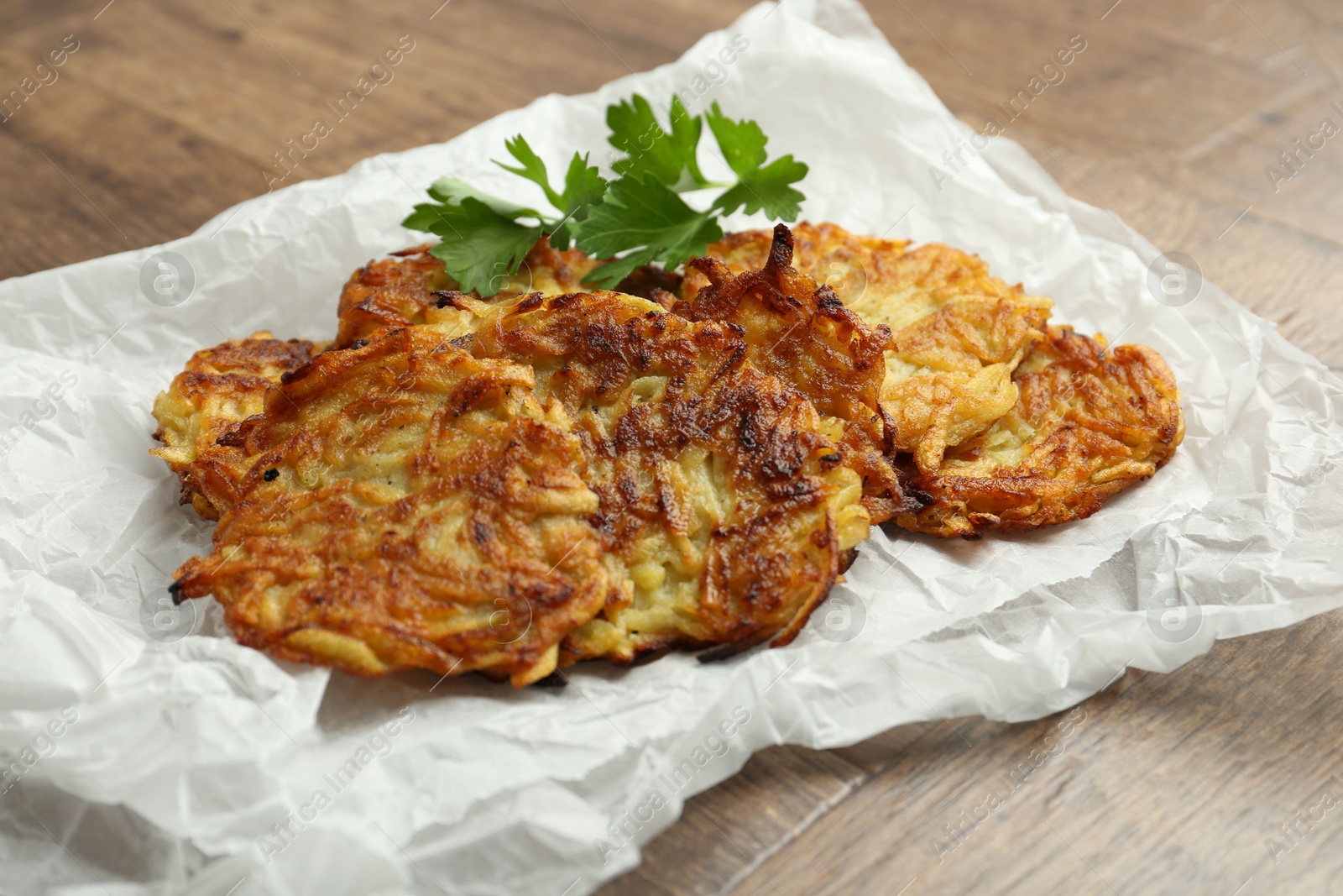 Photo of Delicious potato pancakes and parsley on wooden table, closeup