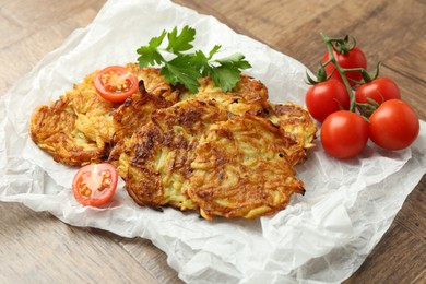 Photo of Delicious potato pancakes, tomatoes and parsley on wooden table, closeup