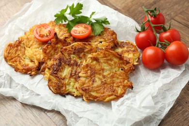 Photo of Delicious potato pancakes, tomatoes and parsley on wooden table, closeup