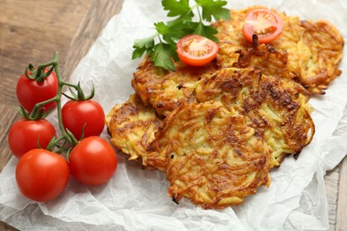 Photo of Delicious potato pancakes, tomatoes and parsley on wooden table, closeup