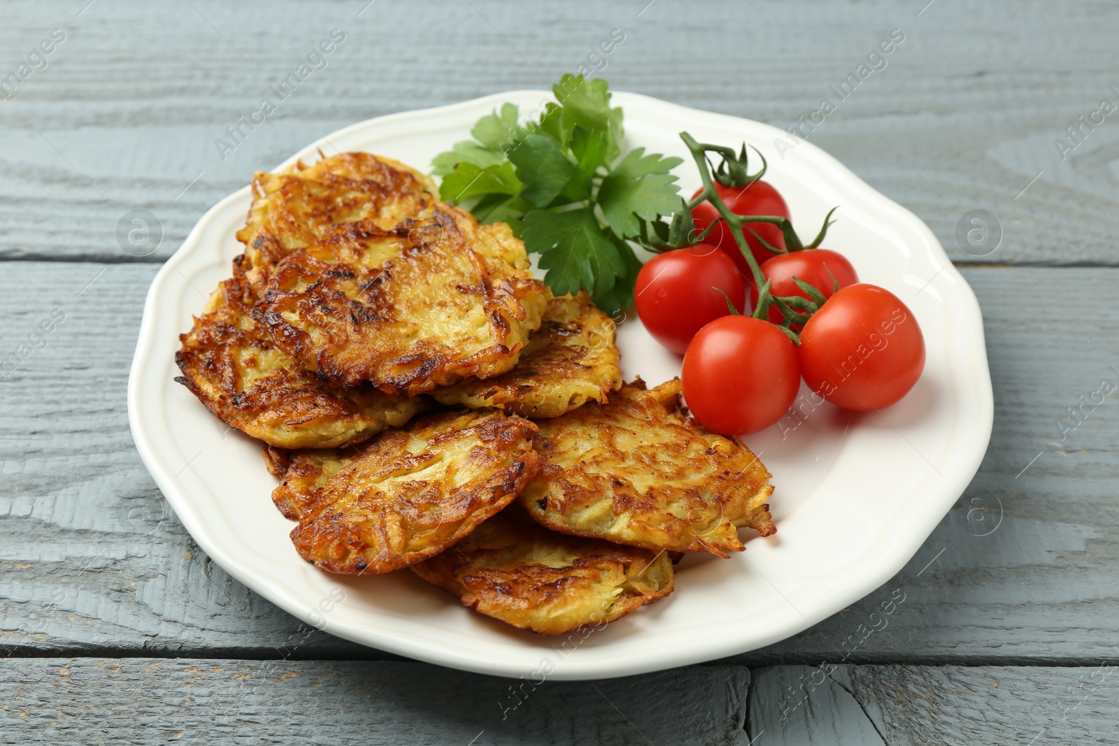 Photo of Delicious potato pancakes, tomatoes and parsley on gray wooden table, closeup