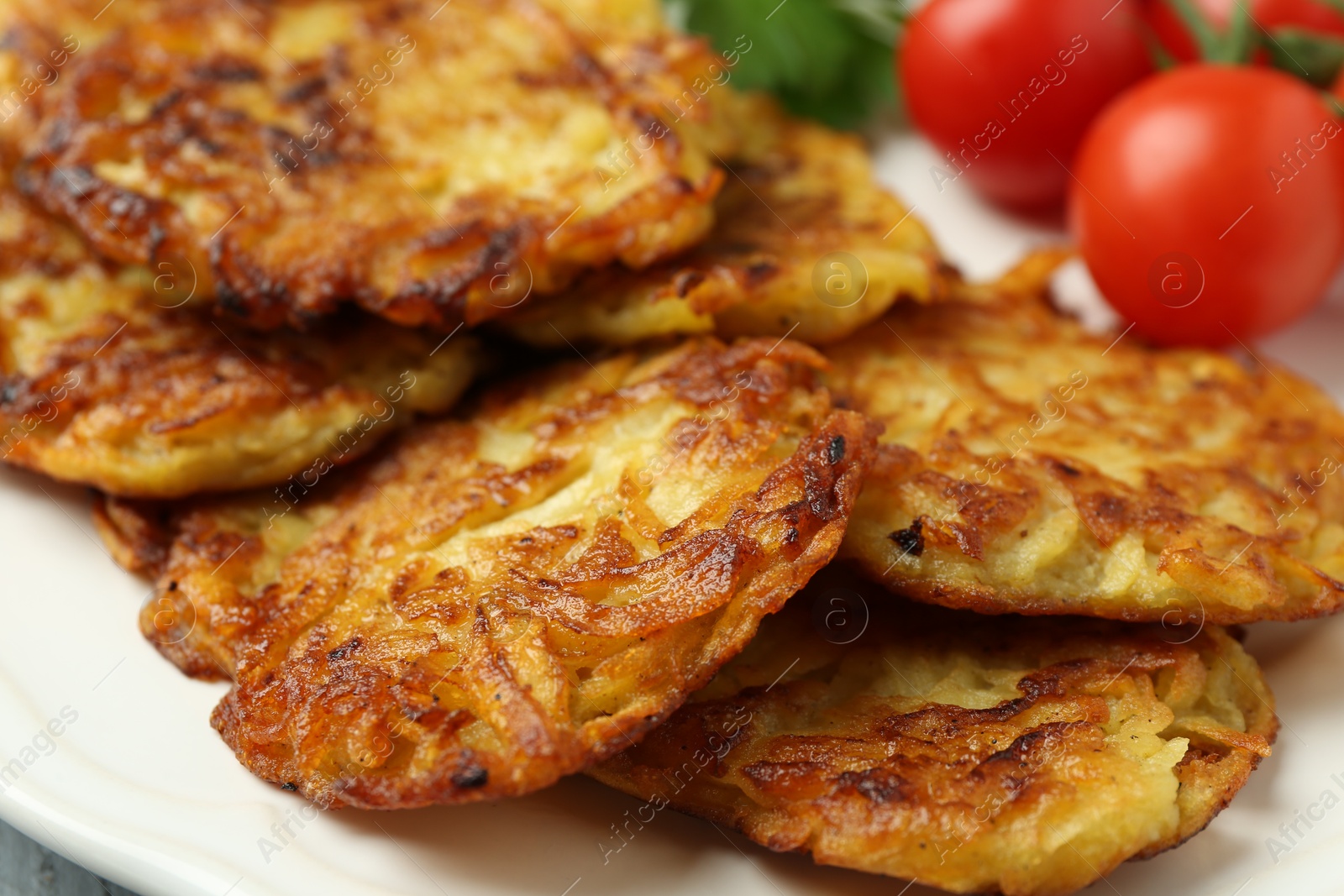 Photo of Delicious potato pancakes, tomatoes and parsley on plate, closeup