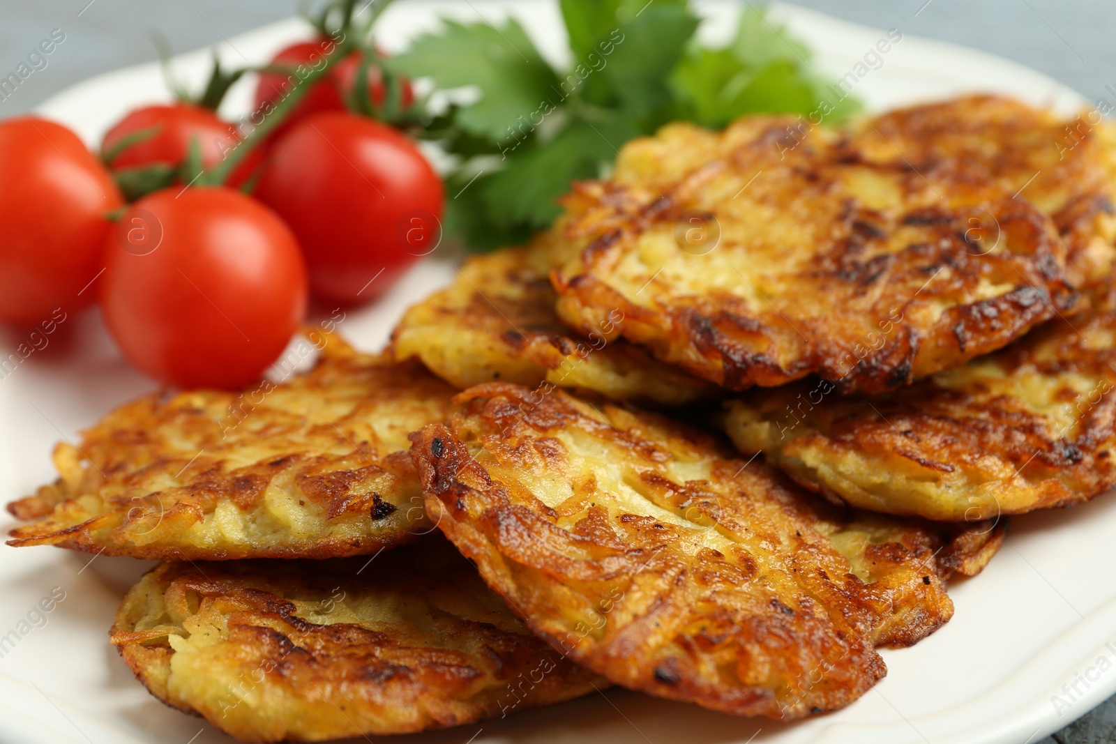 Photo of Delicious potato pancakes, tomatoes and parsley on plate, closeup