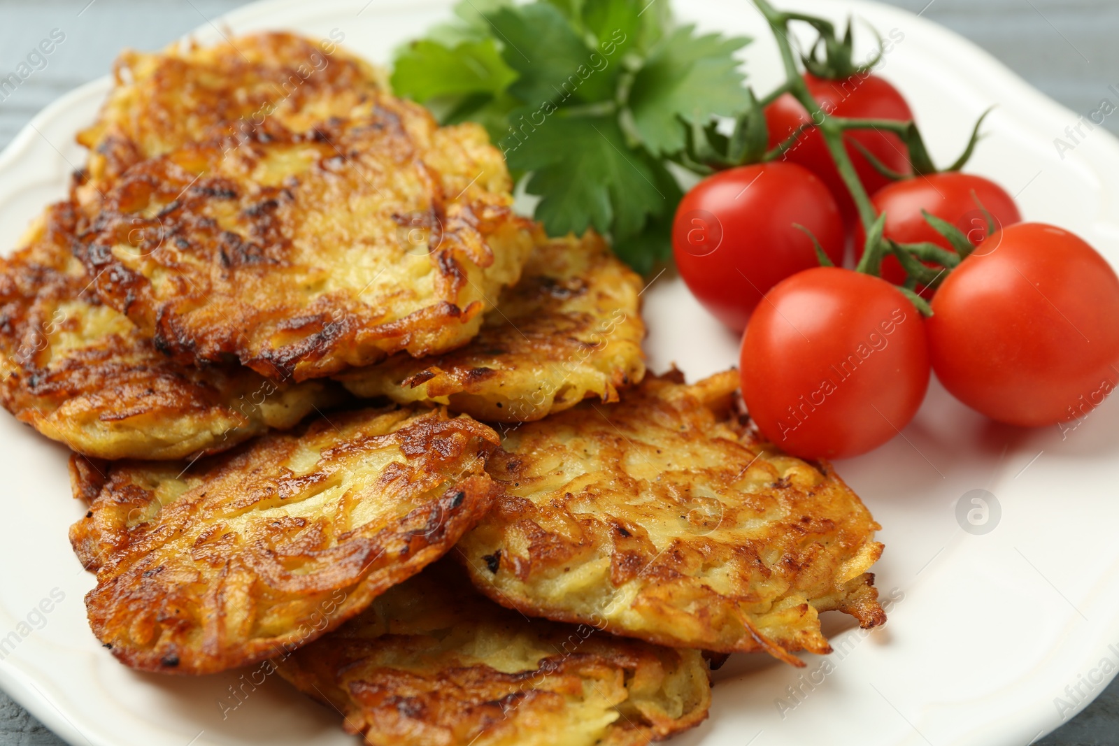 Photo of Delicious potato pancakes, tomatoes and parsley on plate, closeup