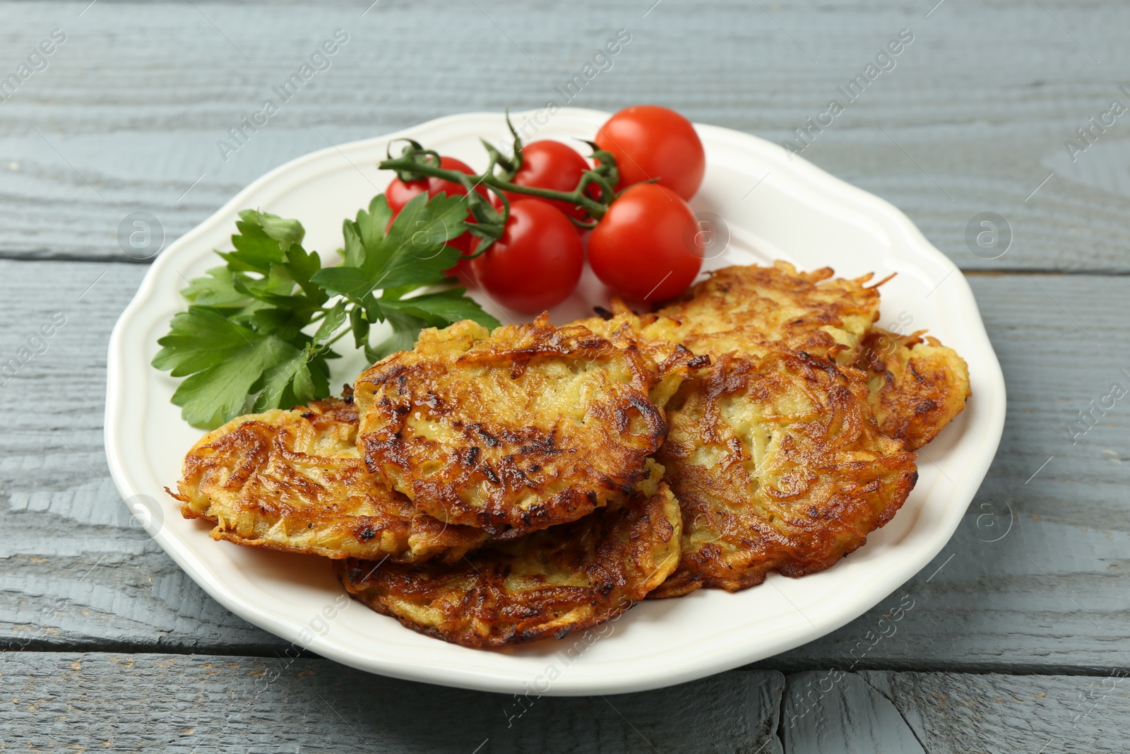 Photo of Delicious potato pancakes, tomatoes and parsley on gray wooden table, closeup