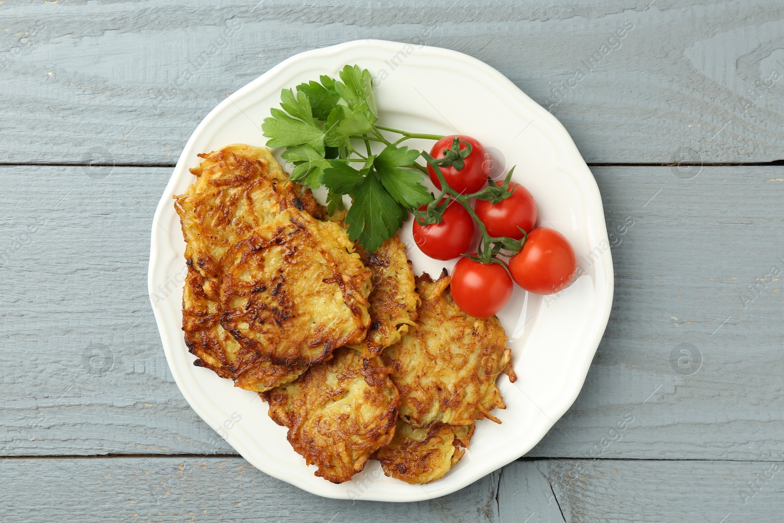 Photo of Delicious potato pancakes, tomatoes and parsley on gray wooden table, top view