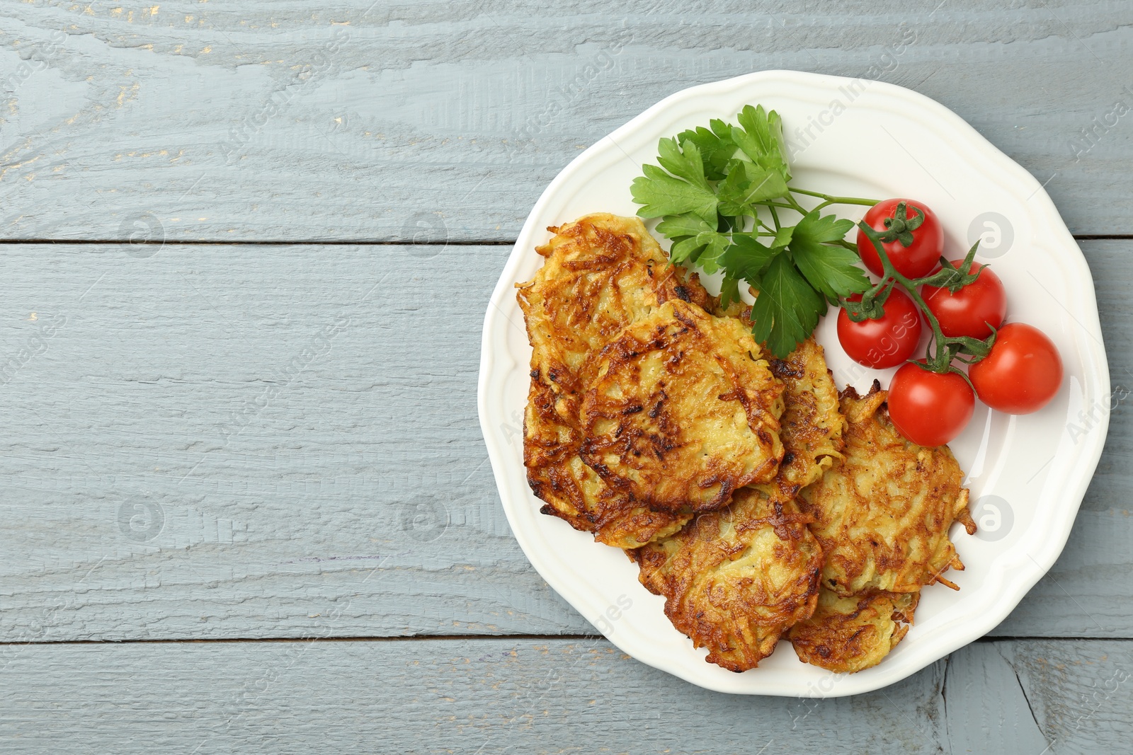 Photo of Delicious potato pancakes, tomatoes and parsley on gray wooden table, top view. Space for text