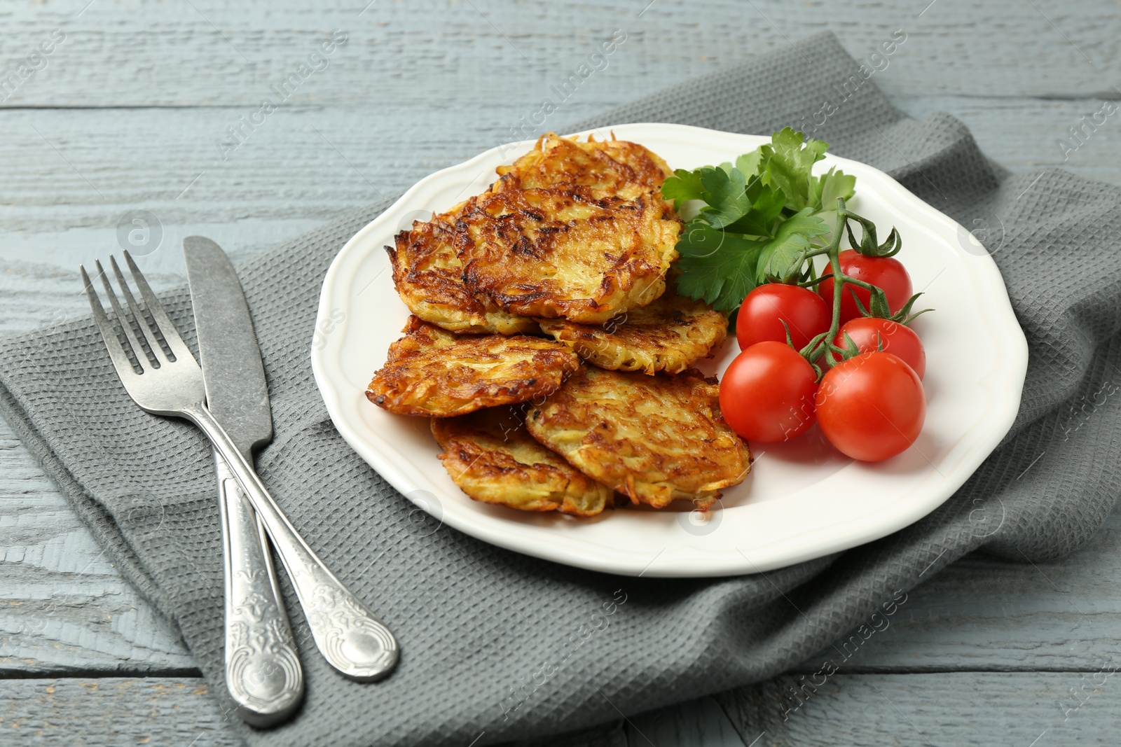 Photo of Delicious potato pancakes with tomatoes and parsley served on gray wooden table, closeup