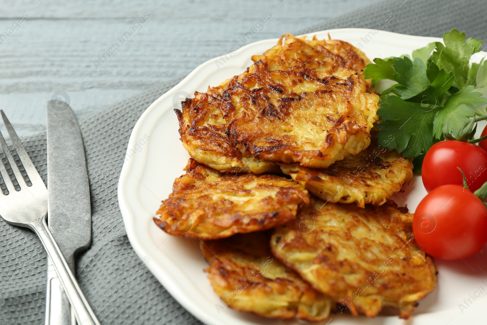 Photo of Delicious potato pancakes with tomatoes and parsley served on gray wooden table, closeup