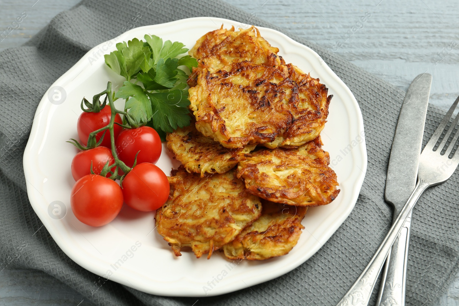 Photo of Delicious potato pancakes with tomatoes and parsley served on gray wooden table, closeup