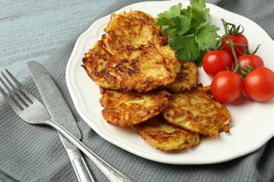 Photo of Delicious potato pancakes with tomatoes and parsley served on gray wooden table, closeup