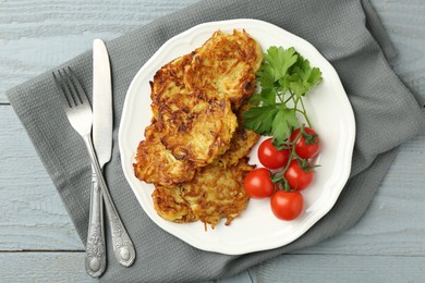 Photo of Delicious potato pancakes with tomatoes and parsley served on gray wooden table, flat lay