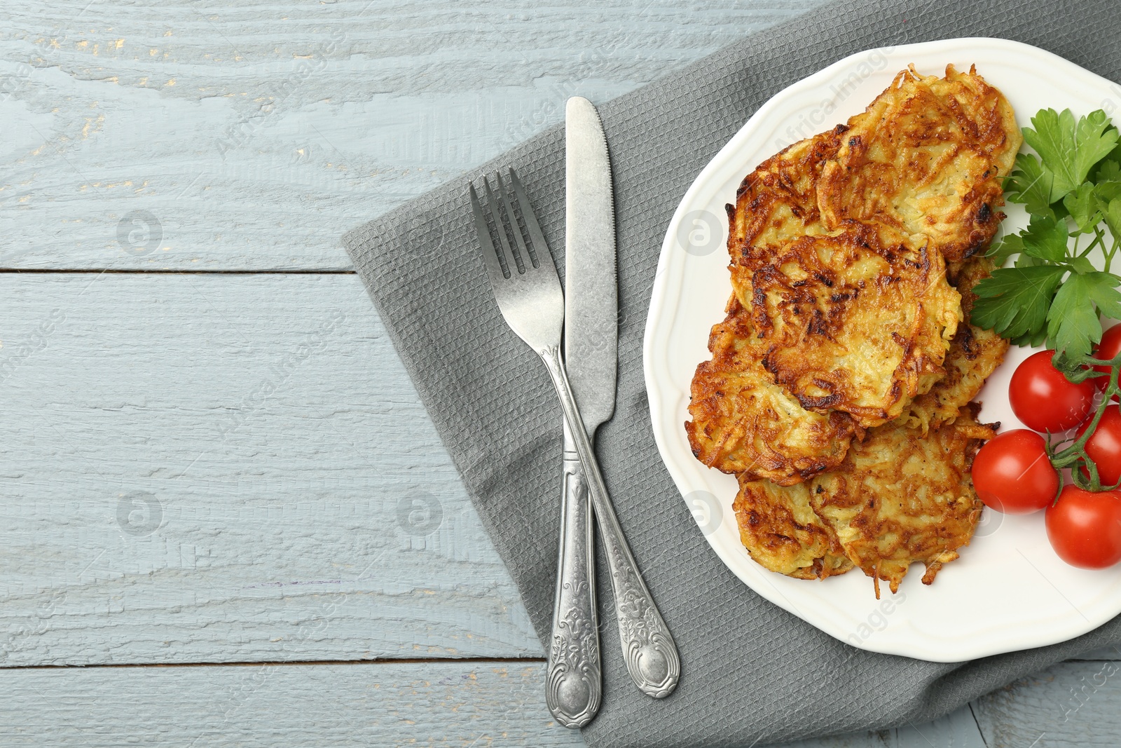 Photo of Delicious potato pancakes with tomatoes and parsley served on gray wooden table, flat lay. Space for text