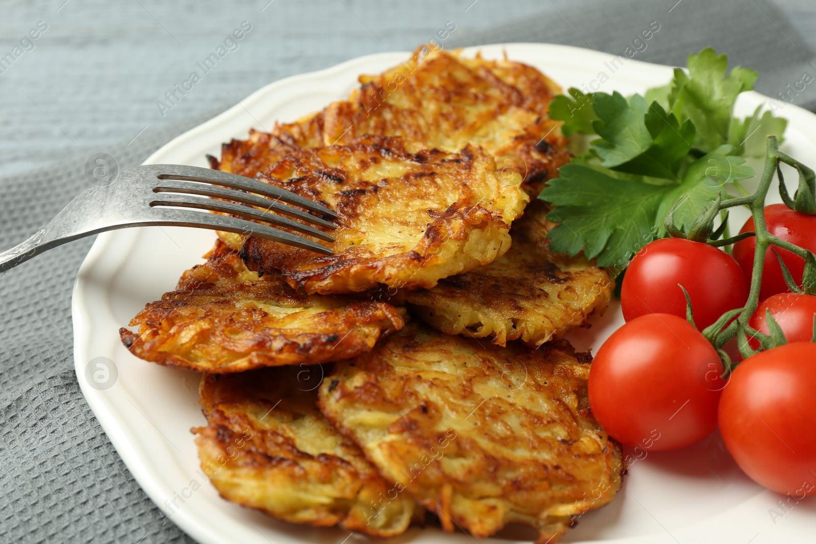 Photo of Delicious potato pancakes with tomatoes and parsley served on gray table, closeup