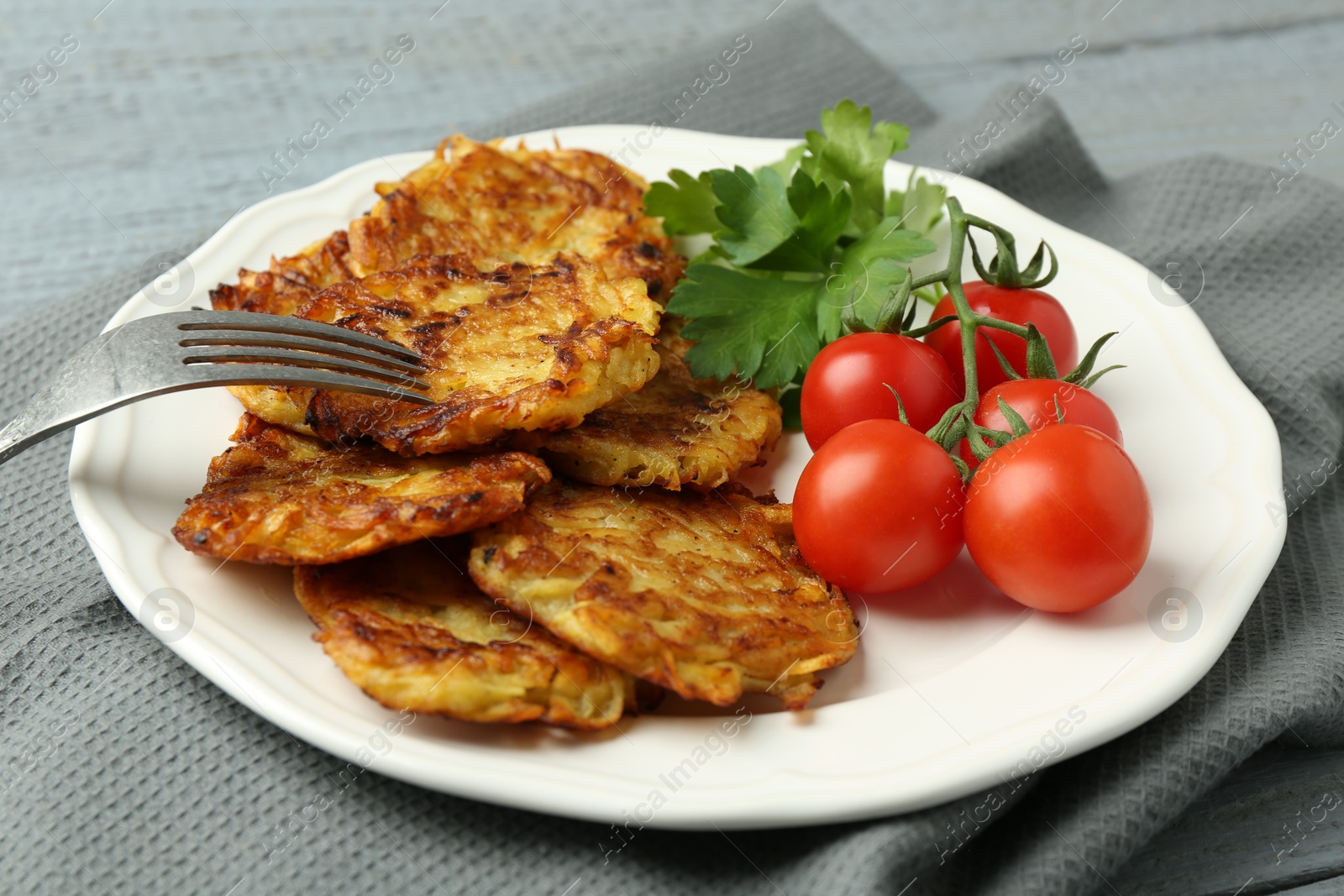 Photo of Delicious potato pancakes with tomatoes and parsley served on gray table, closeup