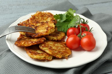 Photo of Delicious potato pancakes with tomatoes and parsley served on gray table, closeup