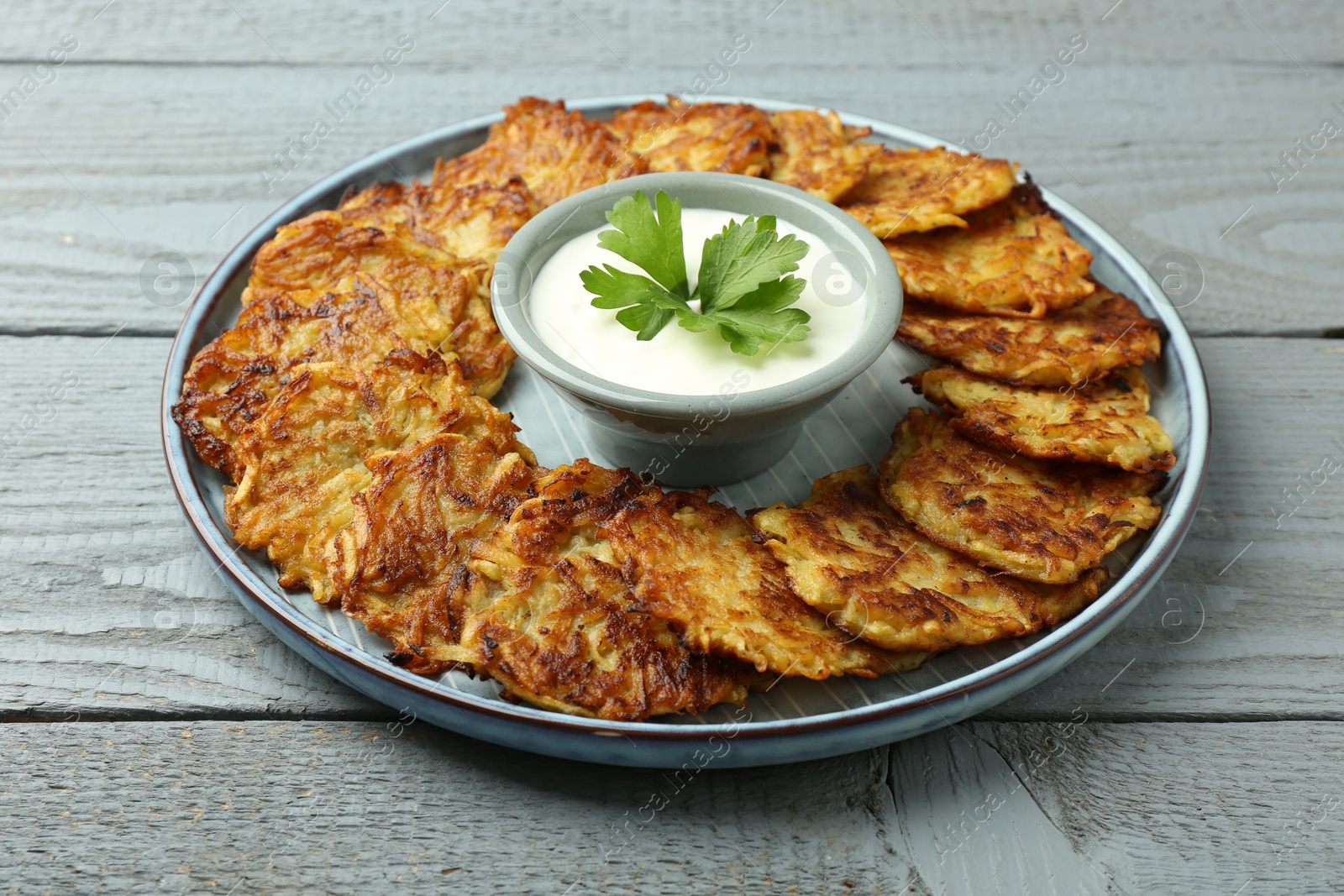 Photo of Delicious potato pancakes and sour cream on gray wooden table, closeup