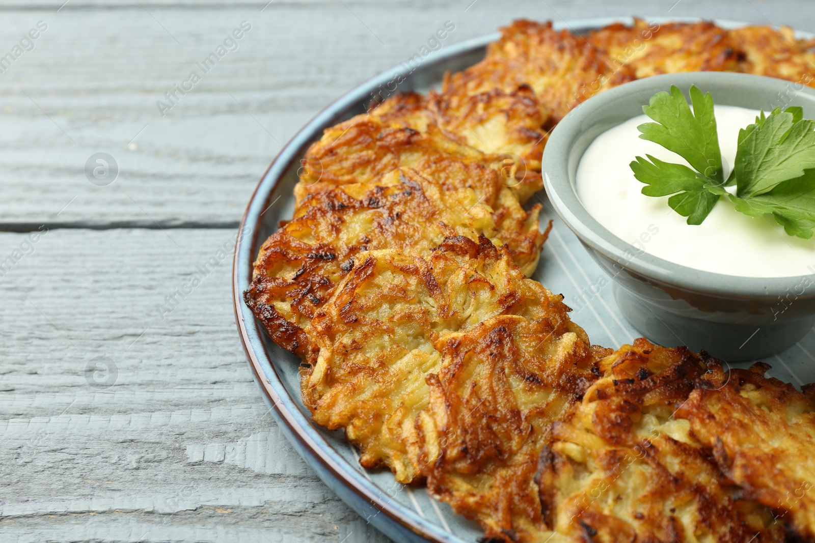 Photo of Delicious potato pancakes and sour cream on gray wooden table, closeup