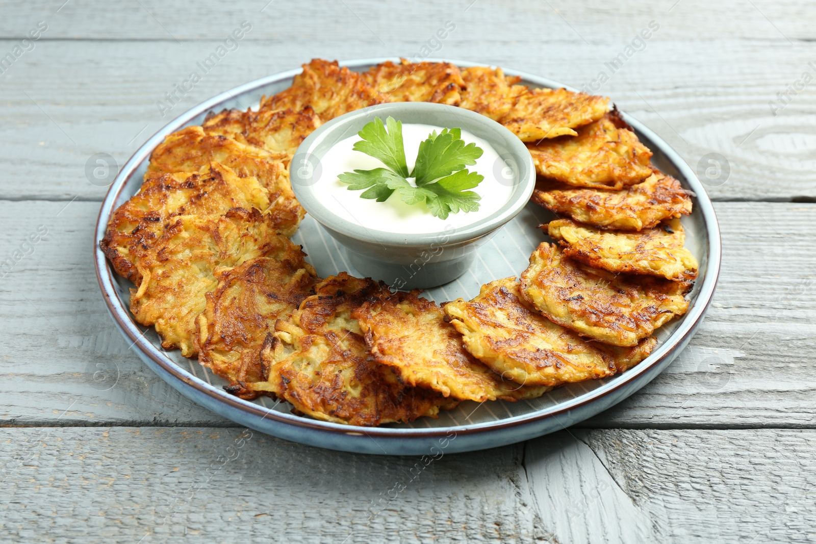 Photo of Delicious potato pancakes and sour cream on gray wooden table, closeup