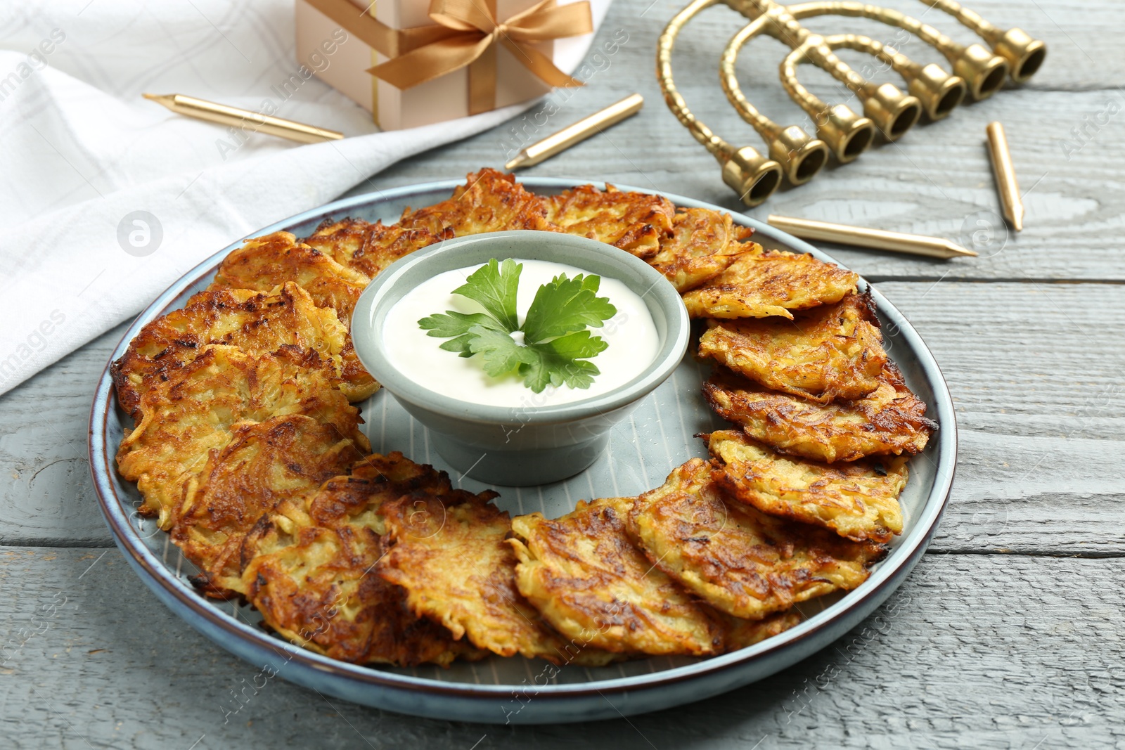 Photo of Delicious potato pancakes, menorah and gift box on gray wooden table, closeup. Hanukkah festive food