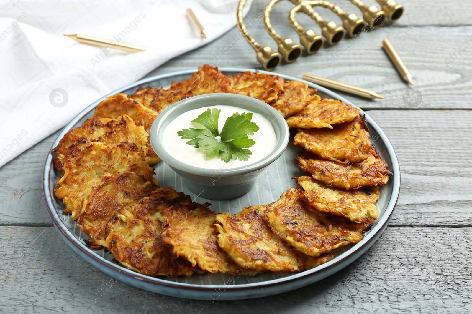 Photo of Delicious potato pancakes, menorah and candles on gray wooden table, closeup. Hanukkah festive food