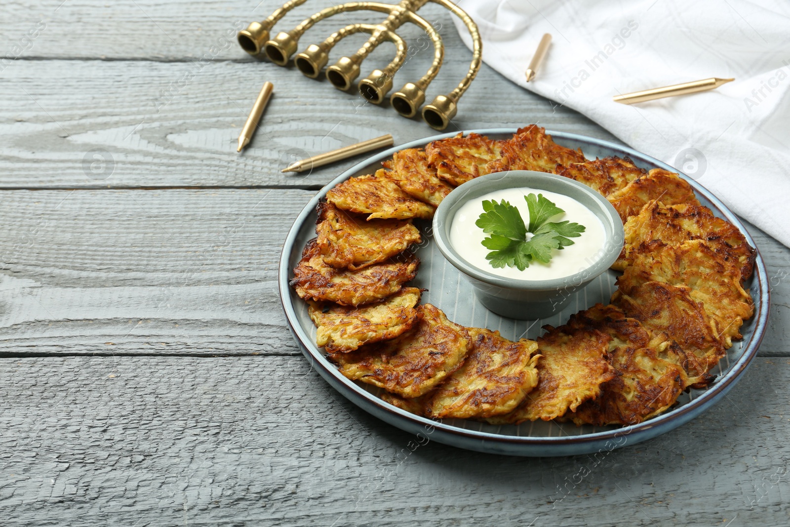 Photo of Delicious potato pancakes, menorah and candles on gray wooden table, closeup. Hanukkah festive food