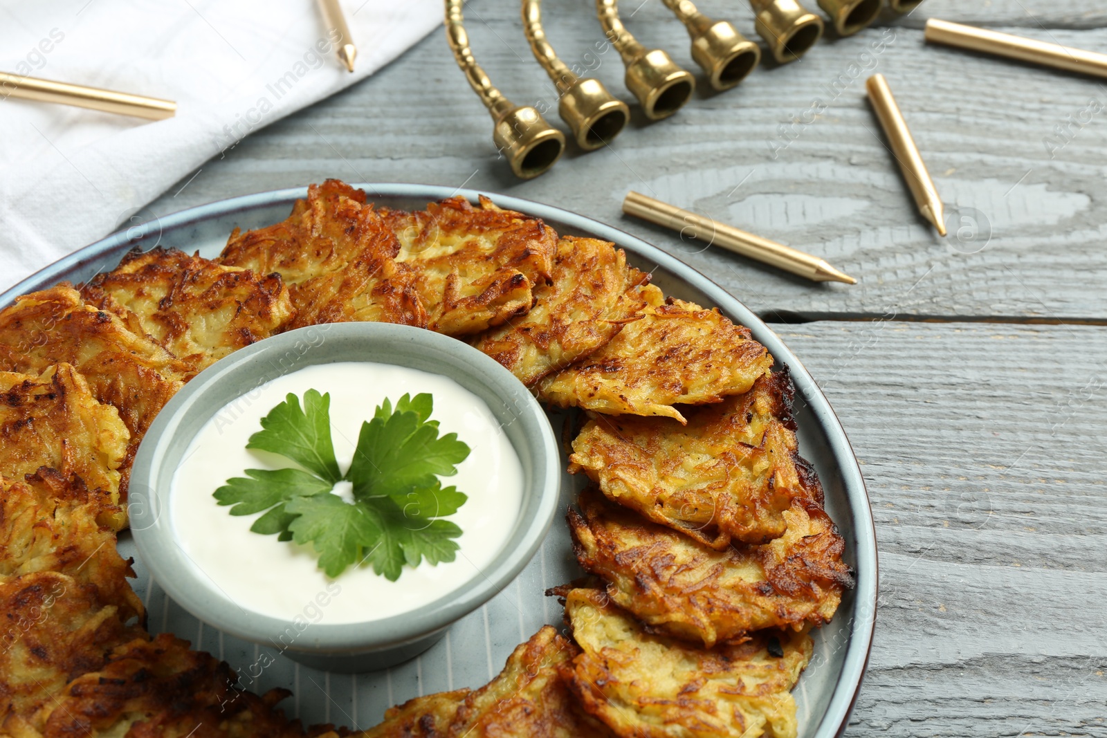 Photo of Delicious potato pancakes, menorah and candles on gray wooden table, closeup. Hanukkah festive food