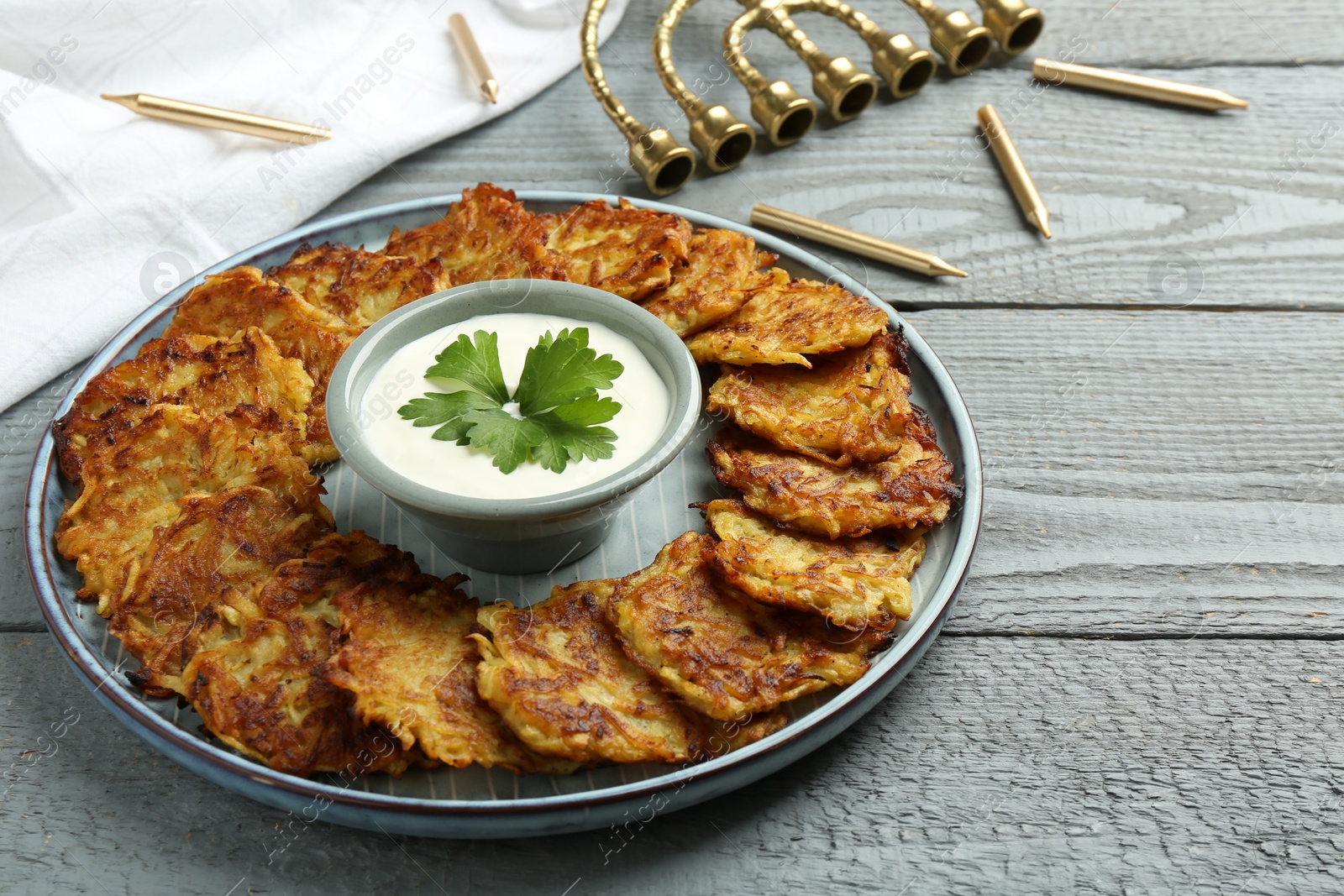 Photo of Delicious potato pancakes, menorah and candles on gray wooden table, closeup. Hanukkah festive food