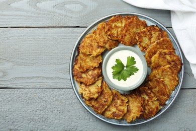 Photo of Delicious potato pancakes and sour cream on gray wooden table, top view. Space for text