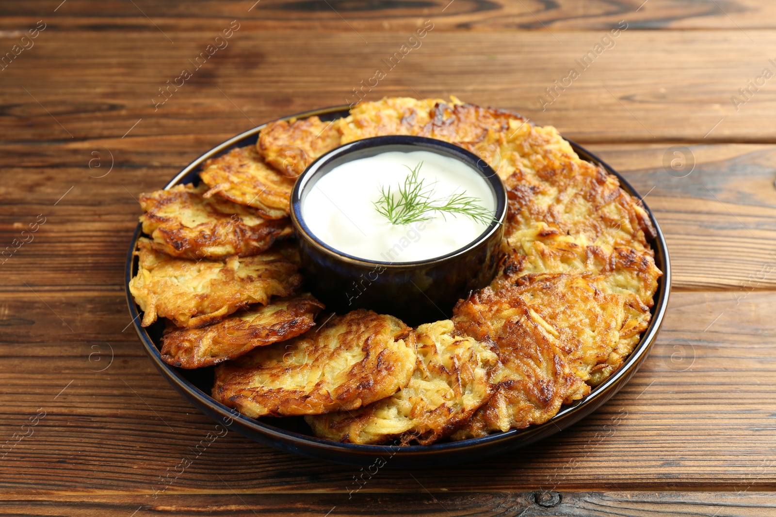 Photo of Delicious potato pancakes with sour cream on wooden table, closeup