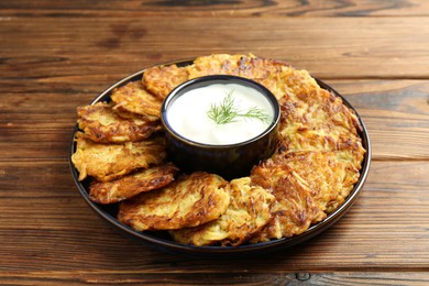 Delicious potato pancakes with sour cream on wooden table, closeup