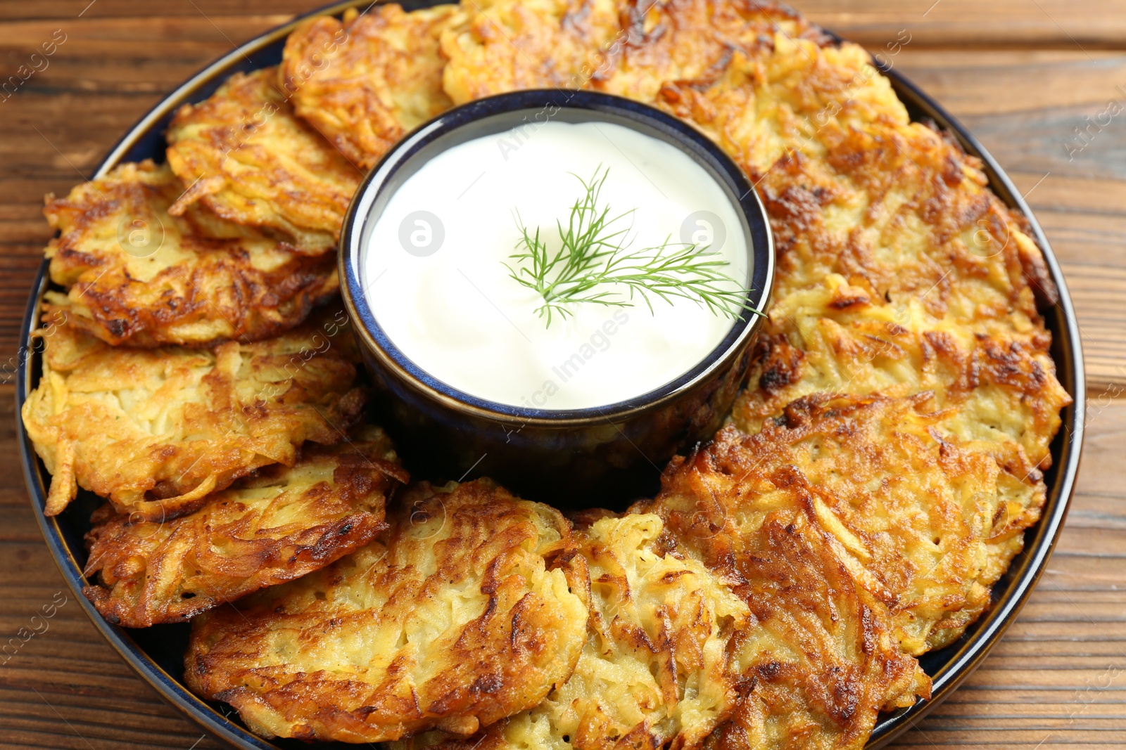 Photo of Delicious potato pancakes with sour cream on wooden table, closeup