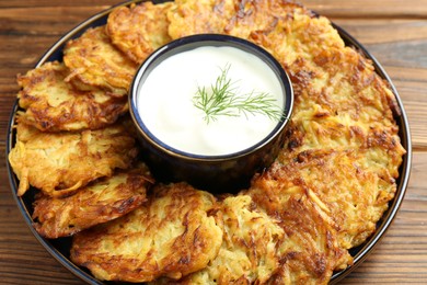 Photo of Delicious potato pancakes with sour cream on wooden table, closeup