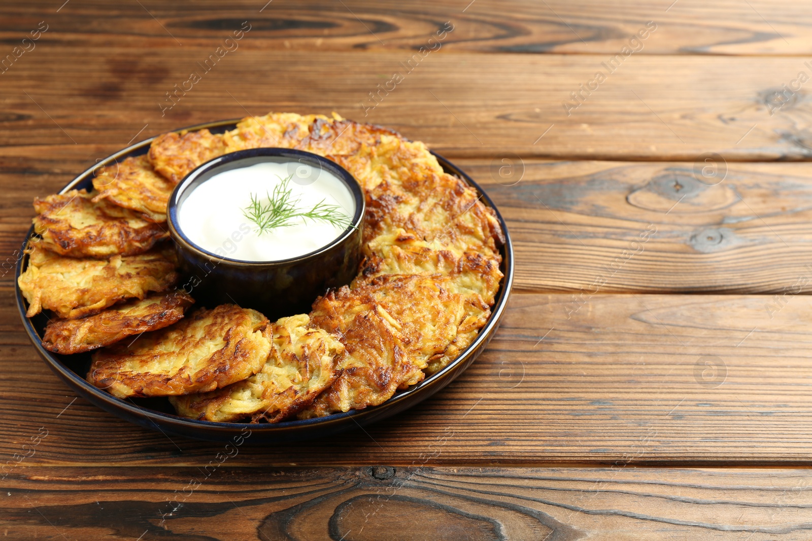 Photo of Delicious potato pancakes with sour cream on wooden table, space for text