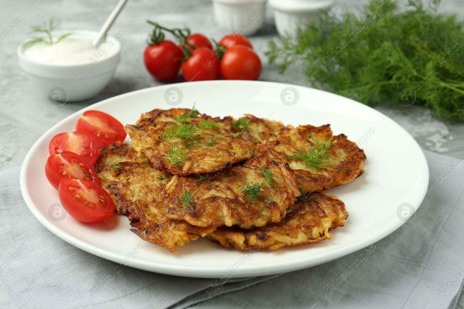 Photo of Delicious potato pancakes with fresh tomatoes served on grey table, closeup