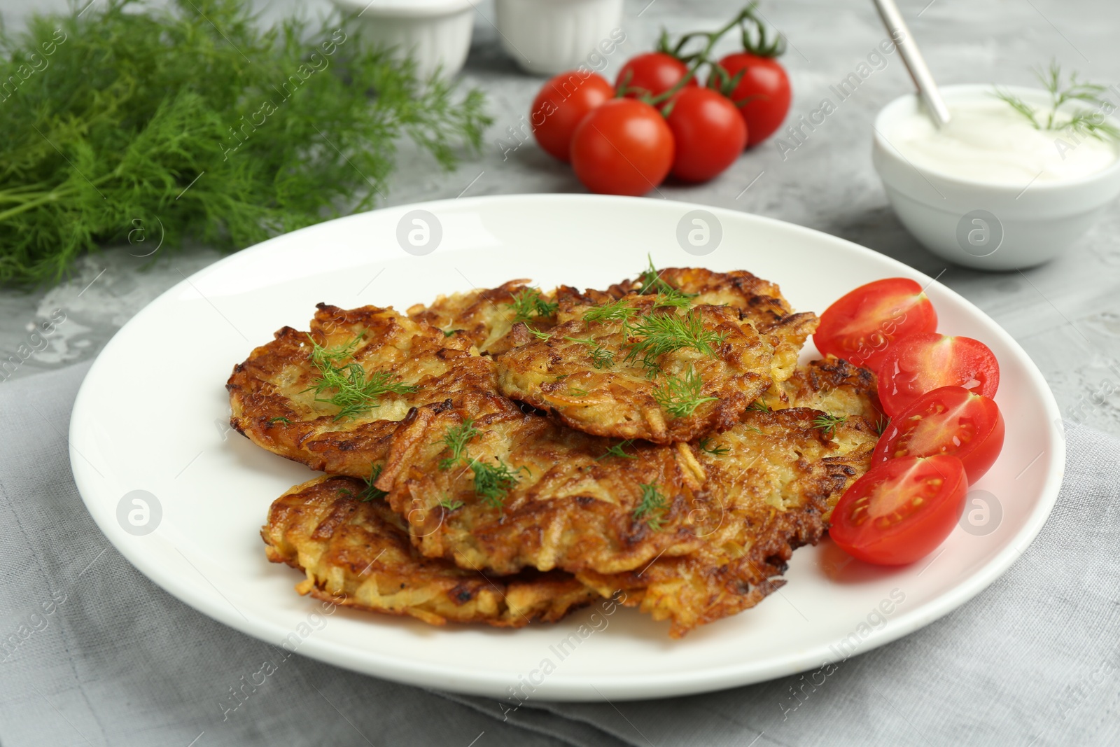 Photo of Delicious potato pancakes with fresh tomatoes served on grey table, closeup