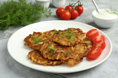 Photo of Delicious potato pancakes with fresh tomatoes served on grey table, closeup