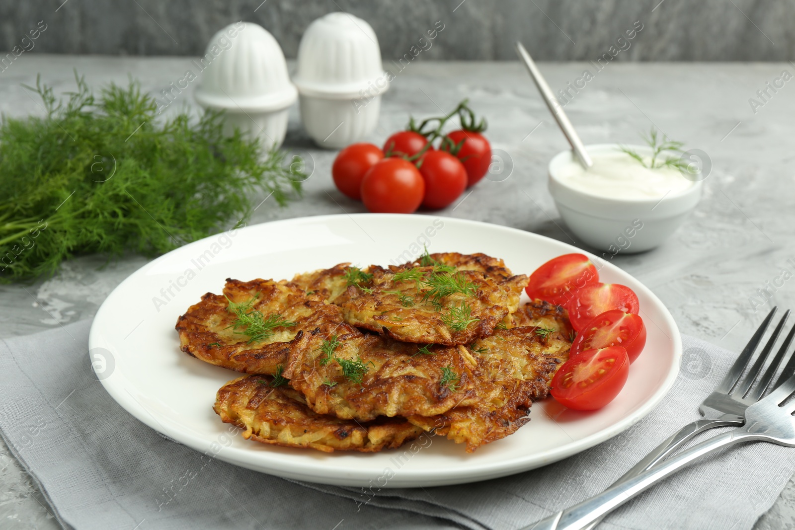 Photo of Delicious potato pancakes with fresh tomatoes served on grey table