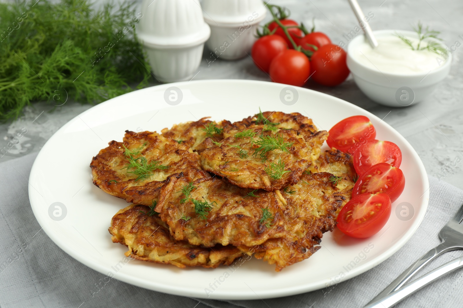 Photo of Delicious potato pancakes with fresh tomatoes served on grey table