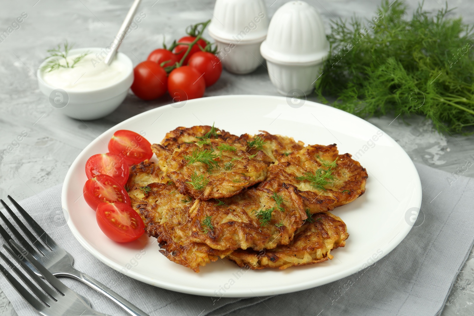 Photo of Delicious potato pancakes with fresh tomatoes served on grey table