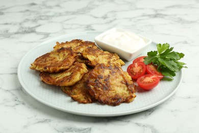 Photo of Delicious potato pancakes with fresh tomatoes, sour cream and parsley on white marble table, closeup