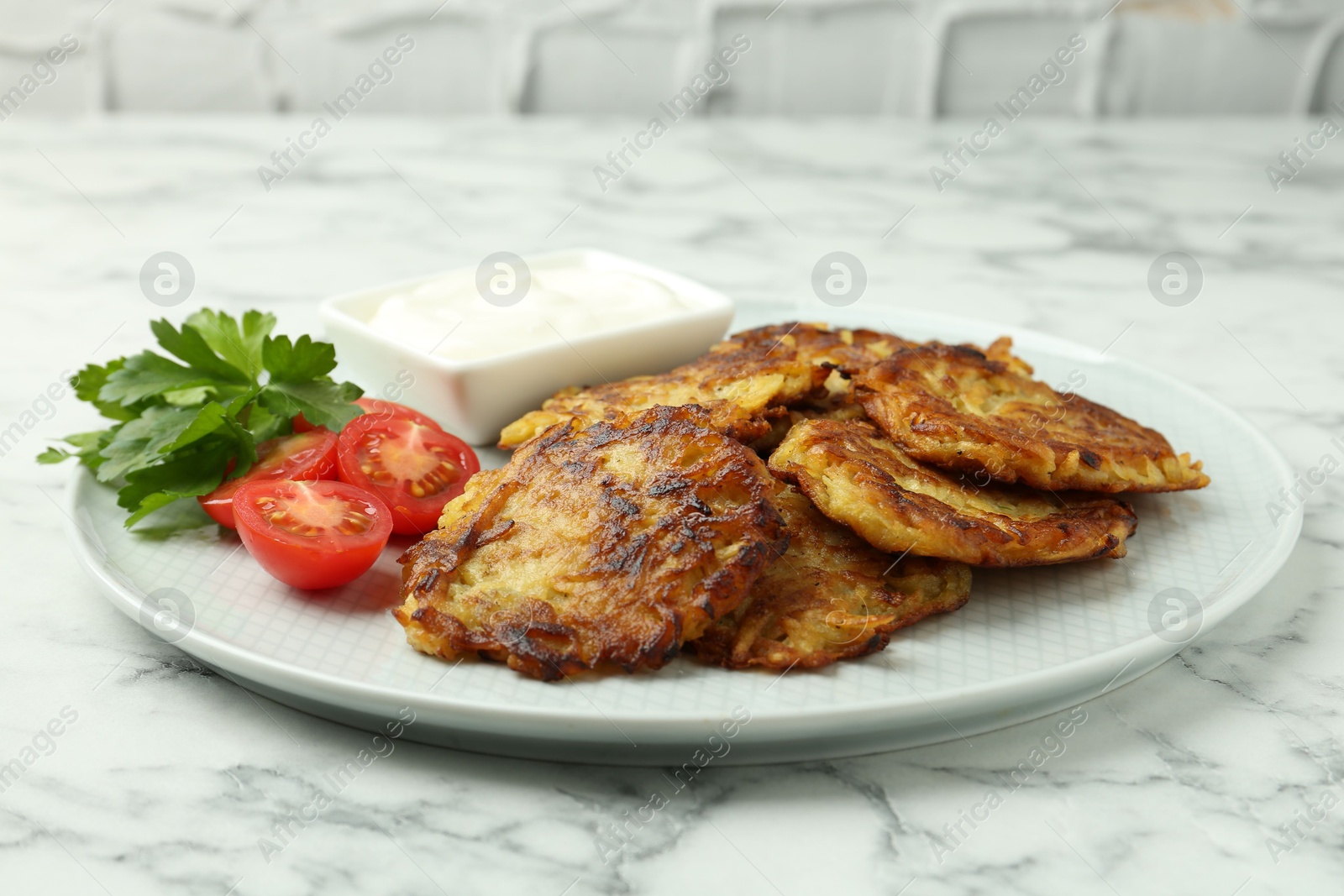 Photo of Delicious potato pancakes with fresh tomatoes, sour cream and parsley on white marble table, closeup