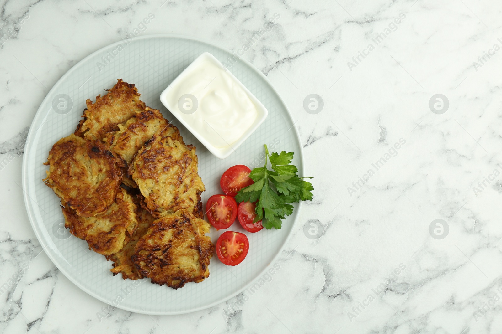 Photo of Delicious potato pancakes with fresh tomatoes, sour cream and parsley on white marble table, top view. Space for text