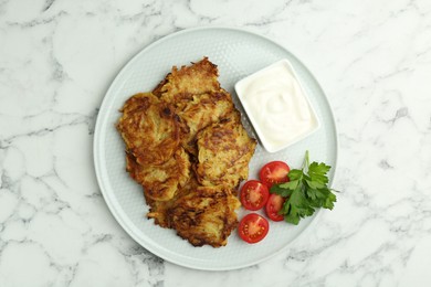 Photo of Delicious potato pancakes with fresh tomatoes, sour cream and parsley on white marble table, top view