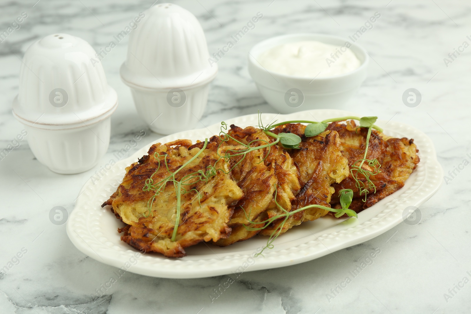 Photo of Delicious potato pancakes with fresh microgreens and sour cream on white marble table, closeup