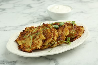 Delicious potato pancakes with fresh microgreens and sour cream on white marble table, closeup